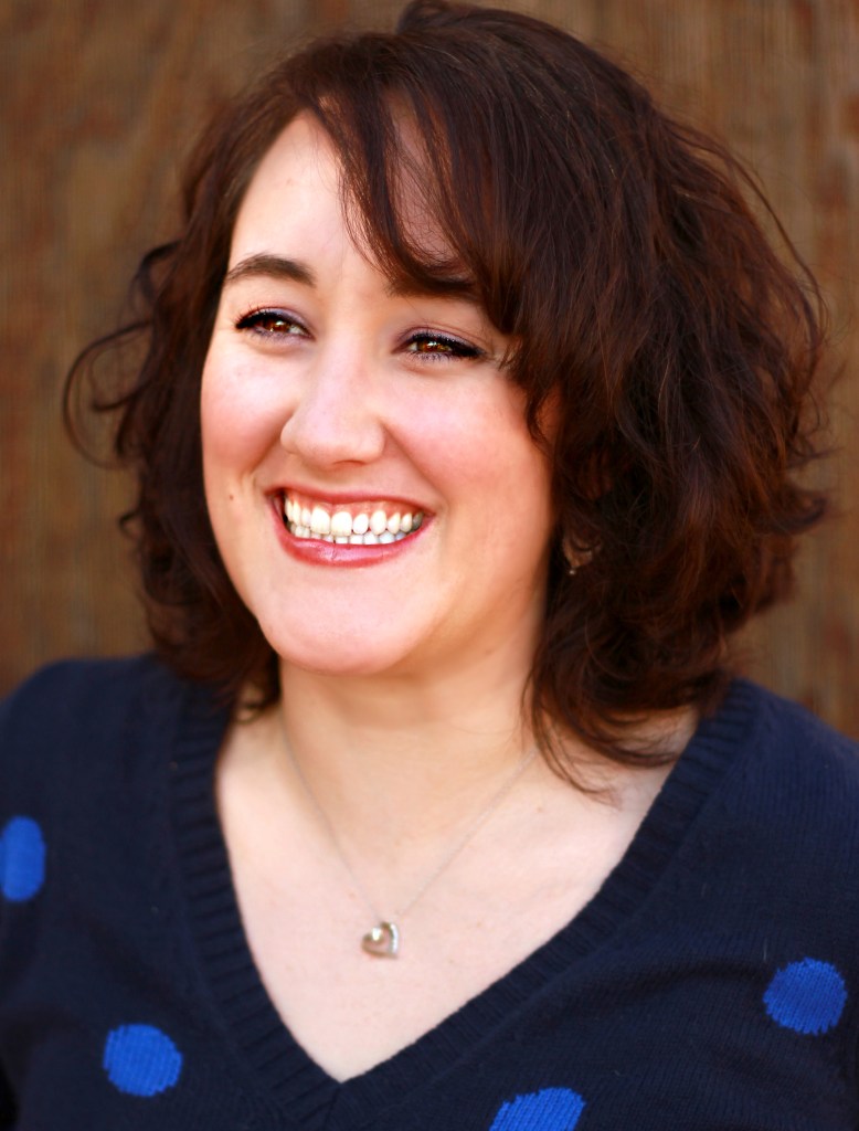 Headshot of Emily smiling in a navy blue sweater with royal blue polka dots.